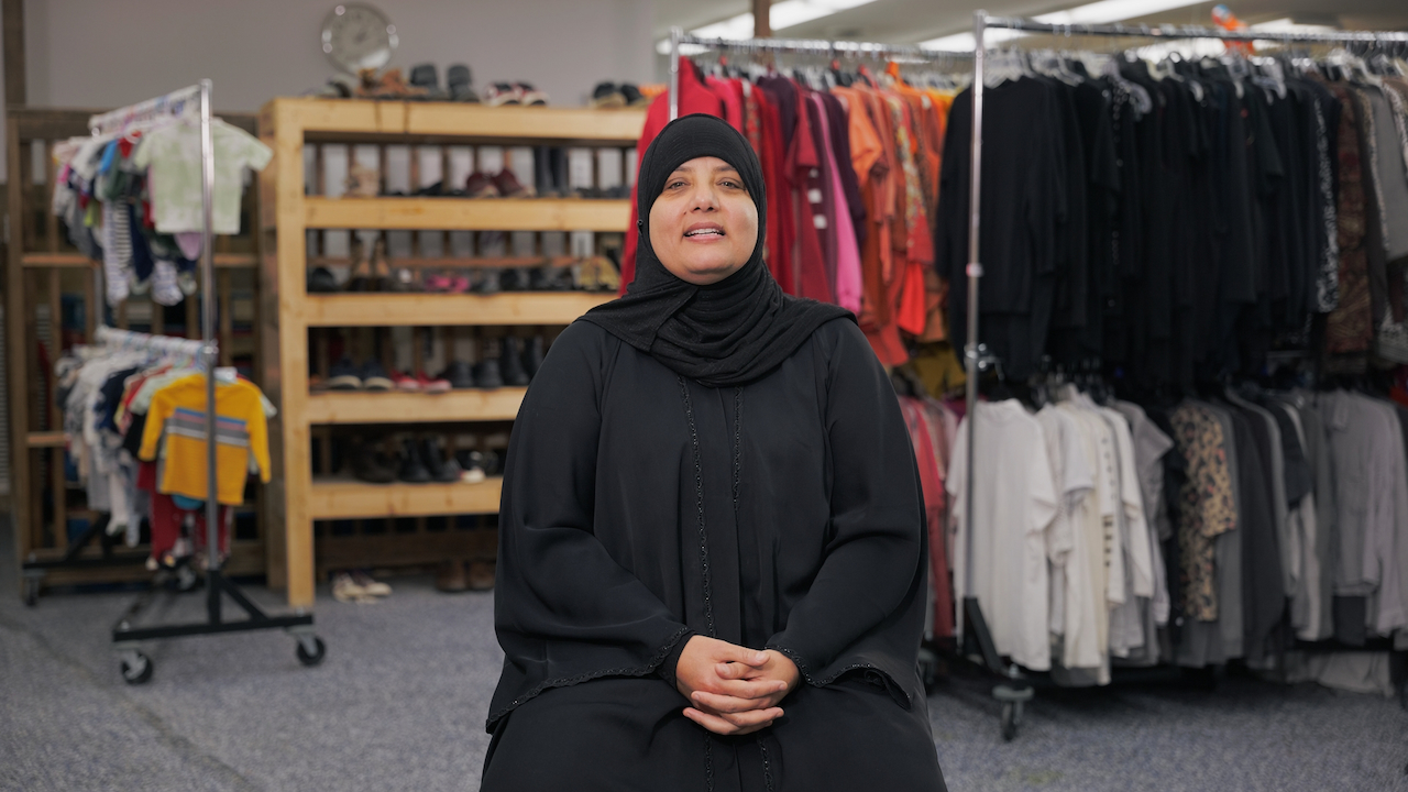 Woman smiling in a black hijab sitting in front of racks of clothing and shelves of shoes