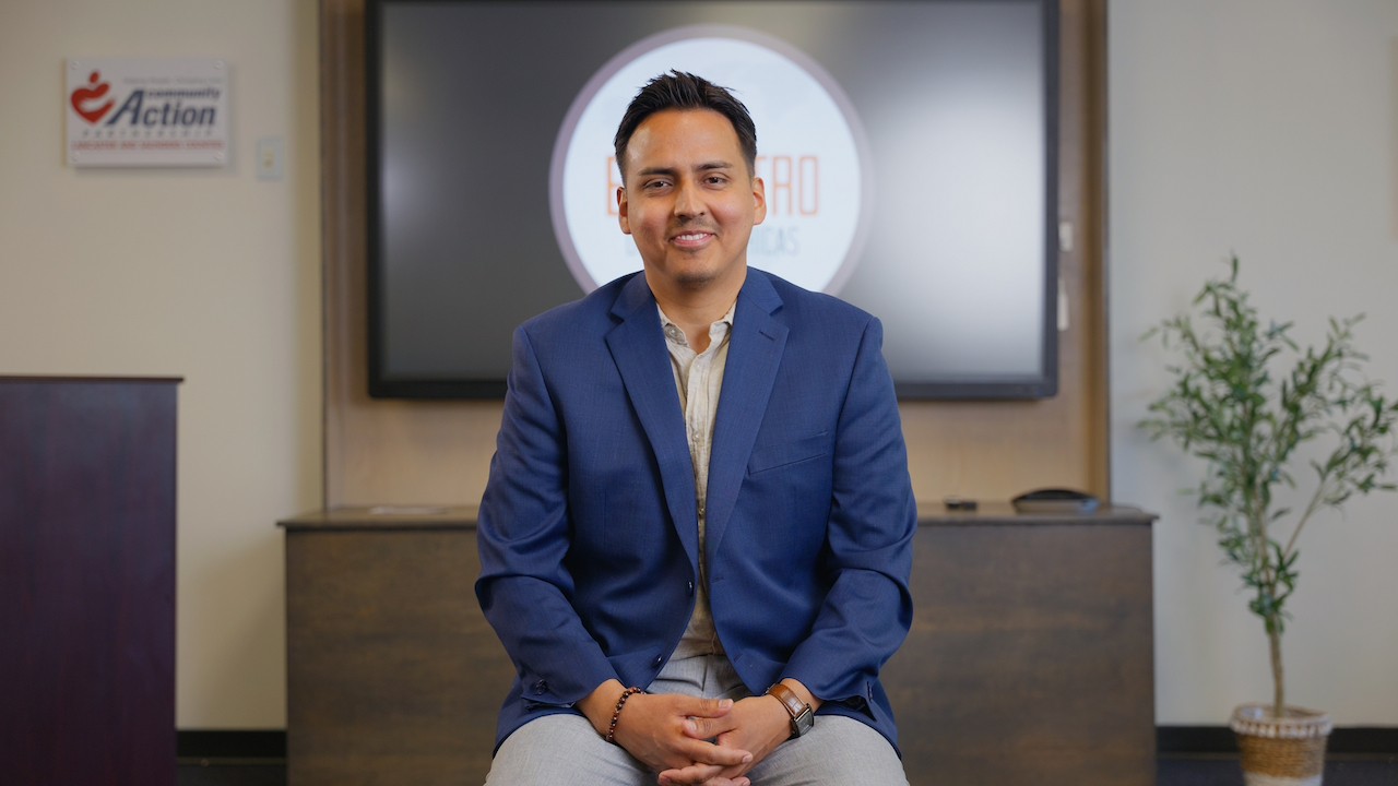 Man with short dark hair smiling wearing a light-colored button down shirt and a navy blue blazer