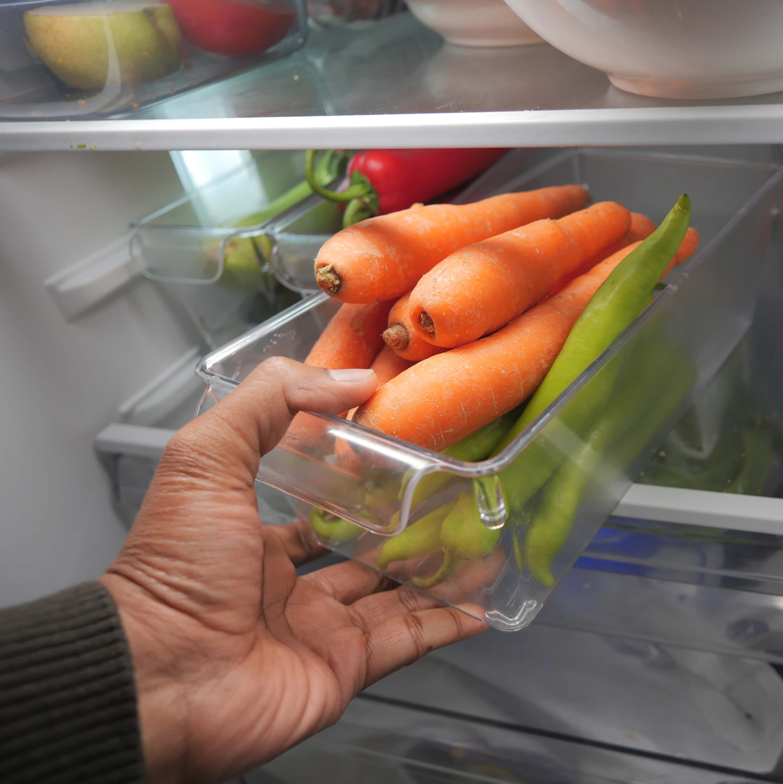 Hand taking a clear bin of carrots out of a fridge