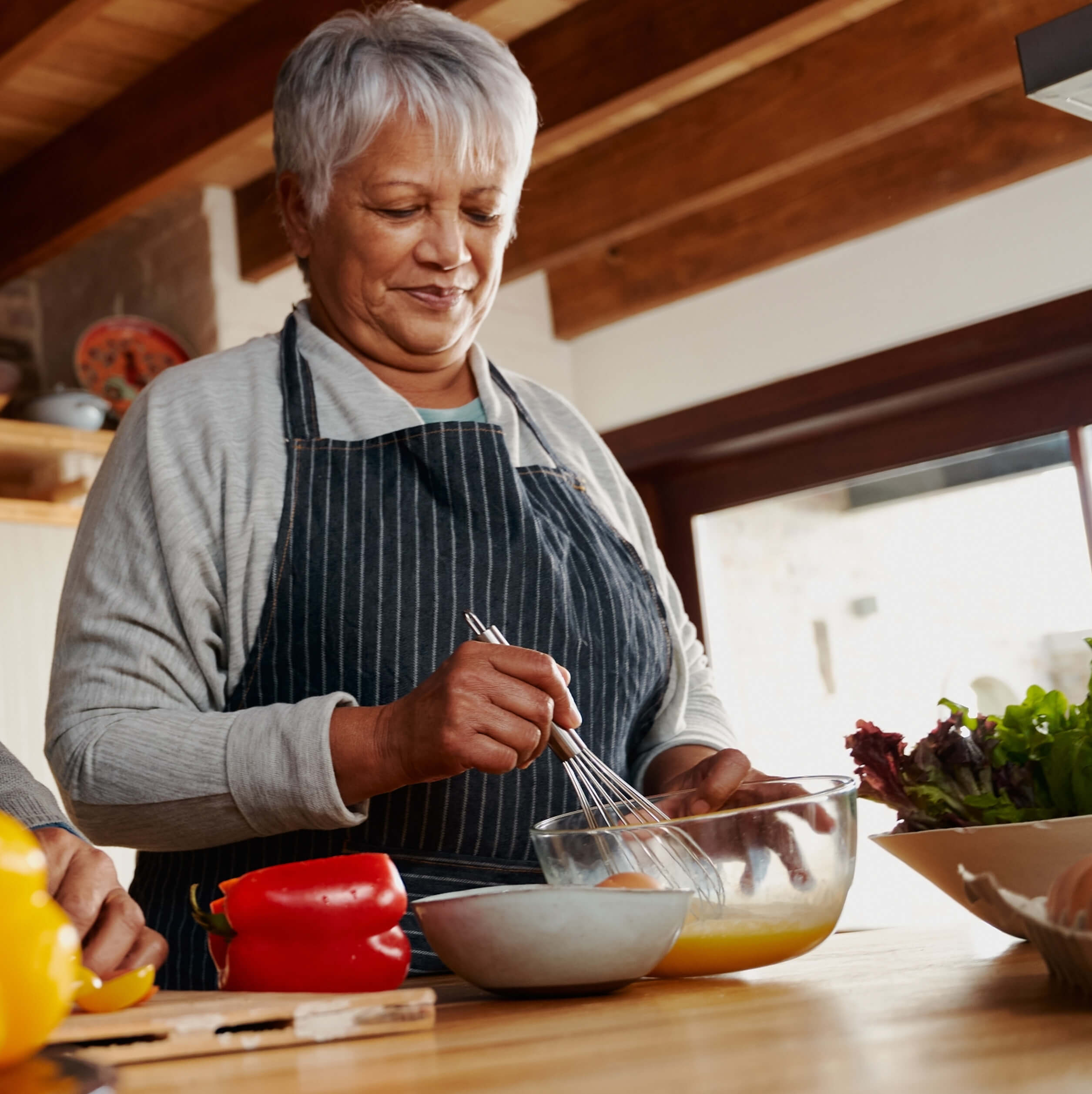 Woman preparing a meal with a whisk and mixing bowl amidst various vegetables